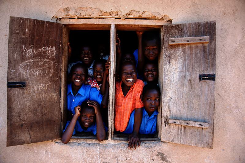 Niños sonriendo asomados a la ventana de una escuela en Camerún
